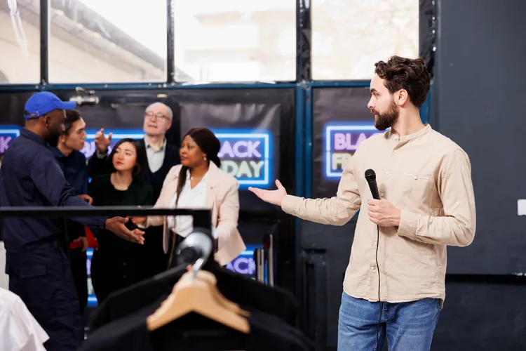 man tv reporter standing shopping mall entrance presenting news about black friday clothing store security guard opening door eager people shoppers waiting discounts seasonal sales